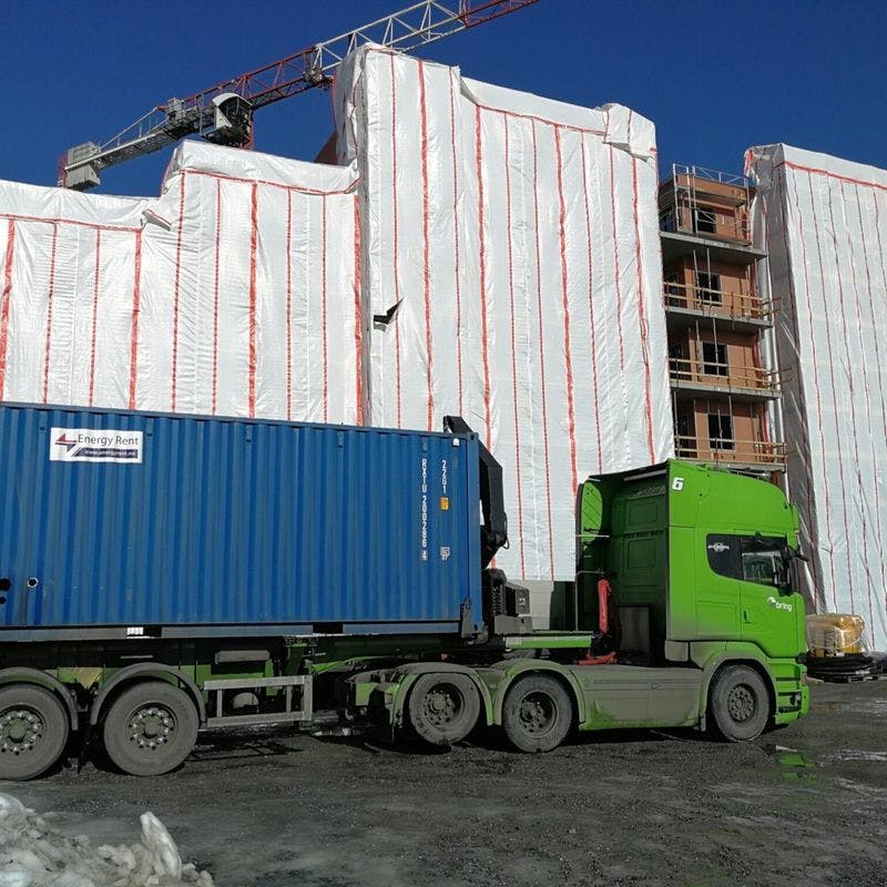 Lastebil med varmecontainer lastet på forrand ett bygg under renovering. 