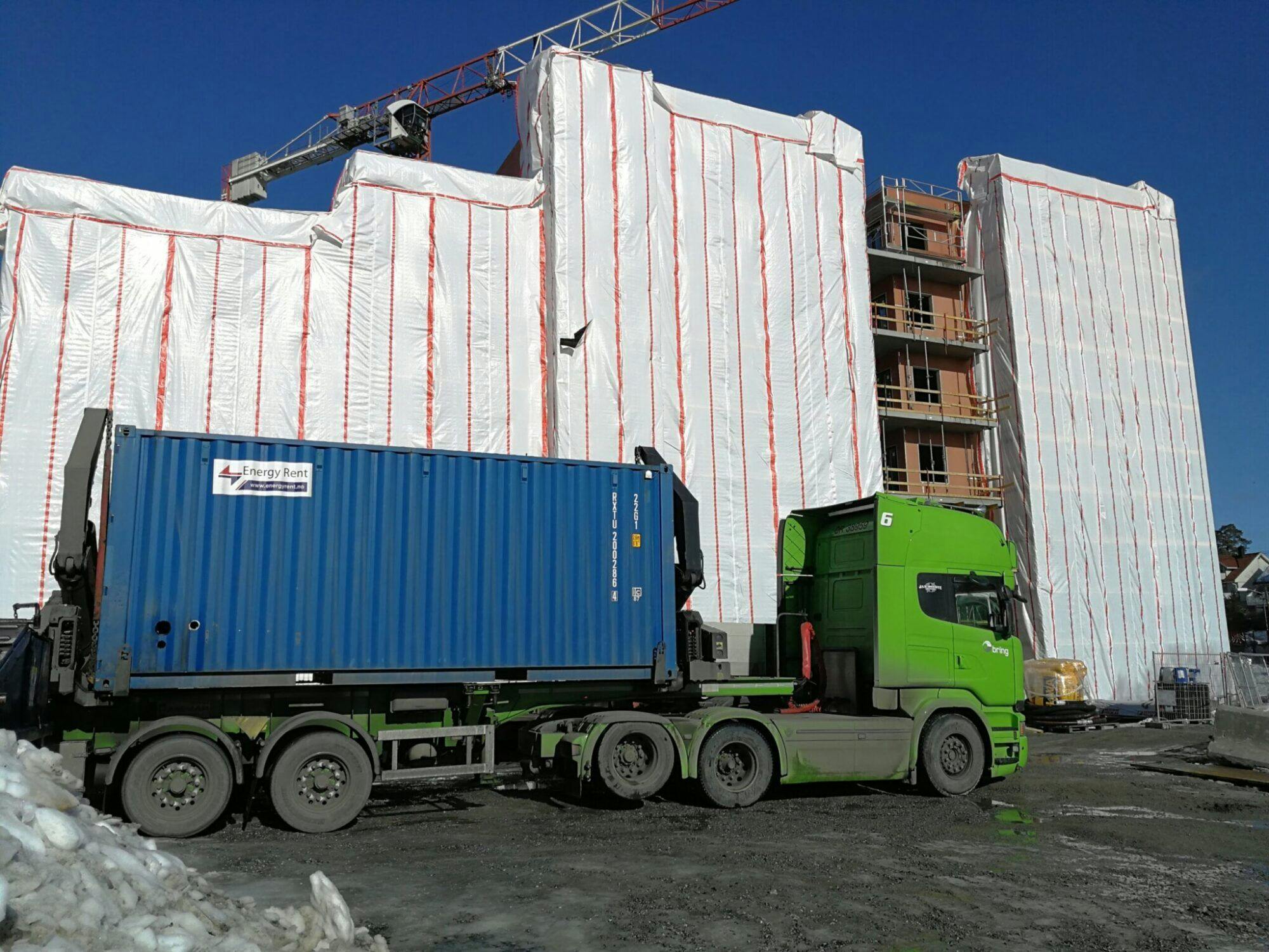 Lastebil med varmecontainer lastet på forrand ett bygg under renovering. 